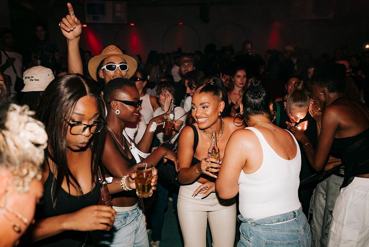 A large group of people dancing and laughing in a club setting. All holding Desperados bottles.