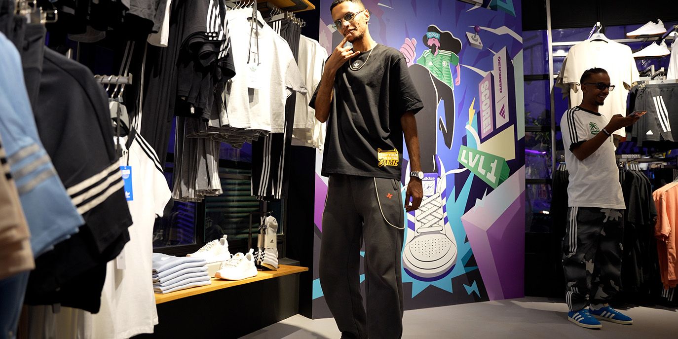 A black man stands inside an adidas retail experience dressed head to toe in adidas's new line of merchandise for esport athletes.